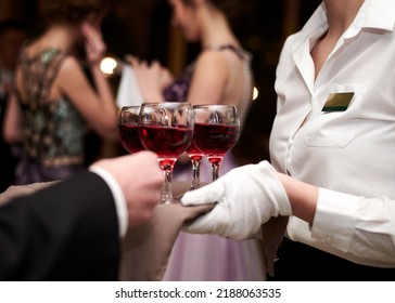 Close-up Picture Of Waiter's Hands Wearing White Gloves Holding A Tray With Red Wine, Serving Alcohol Drinks. Catering Service At Special Occasion, Event. Hospitality Industry Concept.