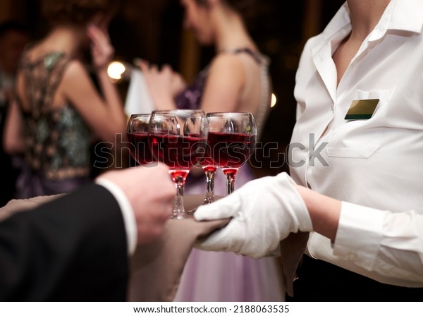 Close-up\
picture of waiter\'s hands wearing white gloves holding a tray with\
red wine, serving alcohol drinks. Catering service at special\
occasion, event. Hospitality industry\
concept.