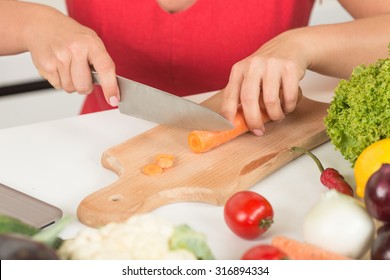 Close-up picture of woman chopping carrot in the kitchen. Lady in red dress demonstarting the correct process of cooking. - Powered by Shutterstock