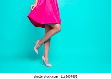 Close-up picture of young girl legs, pink fuchsia short mini dress, walking in high heels shoes. Copy space. Isolated over bright vivid turquoise teal background - Powered by Shutterstock