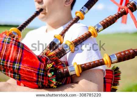Closeup picture of young man playing traditional Scotland bagpipe on green summer outdoors copy space background