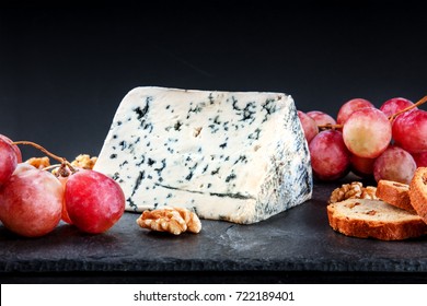 A closeup of a piece of blue cheese with vibrant grapes, slices of bread, and nuts, side view on black textures with a place for text