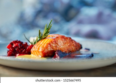 Closeup of piece of delicious red salmon served with fruit garnish on plate in restaurant. Healthy dish cooked in cafe on blurred background. Concept of diet, seafood and protein.