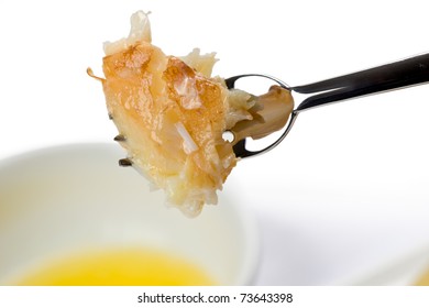 Close-up of a piece of stone crab meat on an appetizer fork with small bowl of melted butter in the background.