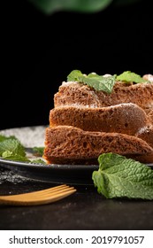 Close-up Of Piece Of Yogurt Sponge Cake With Sugar, Mint Leaves And Fork, Selective Focus, On Wooden Table And Black Background, Vertical