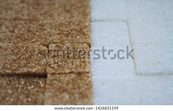 Close-up of pieces of white refined sugar and\
brown cane sugar divide in half\
frame