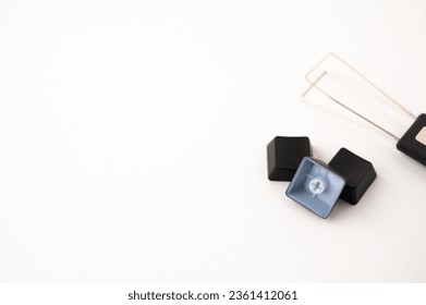 A close-up of a pile of three detached mechanical keyboard keycaps placed near a stainless steal keycap and switch puller tool on a white background. Copy space.