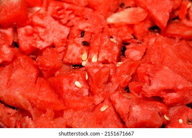 A closeup of a pile of watermelon fruit cuts into small pieces with seeds and without the green shell ready to be served as a healthy fresh snack, selective focus of a stack of  fresh ripe watermelon