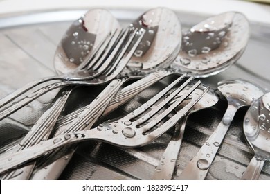 Close-up of a pile of wet silver forks and spoons on a sink