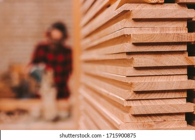 Closeup pile of wooden boards at lumber production factory. Stack of cut plywood at sawmill. Wooden material for furniture production at workshop. Carpenter using electrical circular saw on background