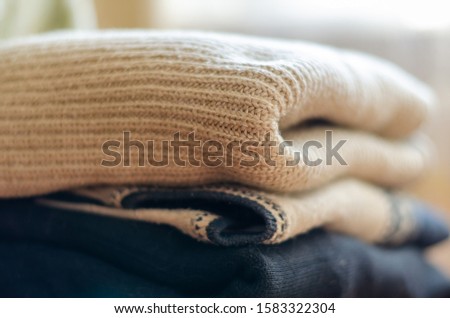 Close-up of a pile of woolen sweaters. Bunch of knitted warm sweaters with different knitting patterns. Fall winter season knitwear. Eye level shooting. Soft focus.
