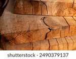 Close-up of piled stack of natural brown uneven rough wooden boards lit by bright sun. Sawmill. Wooden planks at a sawmill or in a carpentry workshop. Sawing and drying of wood. Woodworking industry