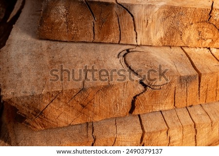 Close-up of piled stack of natural brown uneven rough wooden boards lit by bright sun. Sawmill. Wooden planks at a sawmill or in a carpentry workshop. Sawing and drying of wood. Woodworking industry