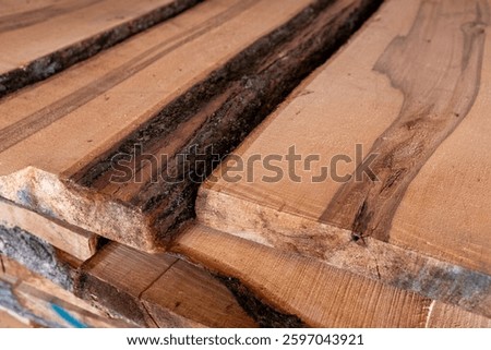 Close-up of piled stack of natural brown uneven rough wooden boards lit by bright sun. Sawmill. Wooden planks at a sawmill or in a carpentry workshop. Raw wood drying in the lumber warehouse