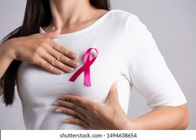 Closeup of pink badge ribbon on woman chest to support breast cancer cause. Healthcare, medicine and breast cancer awareness concept.