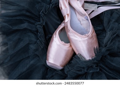 Closeup of the pink ballet pointe shoes laying on the black chiffon Tutu. Two beige ballet slippers on the dark background. Minimalistic concept. Copy Space. Selective focus. - Powered by Shutterstock