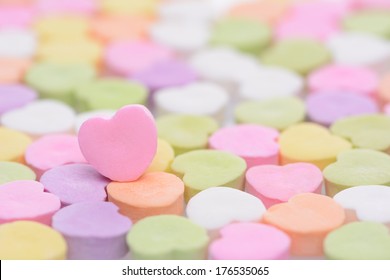 Closeup of a pink candy heart for Valentines Day standing out in a field of out of focus similar candies. Heart is set to one side leaving room for your copy. The candies are blank. 