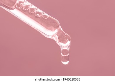 Closeup of pink dropper, falling drop close up. Beauty skin care product. Pipette with essential oil, serum with peptides, hyaluronic acid on pink background. Self care concept