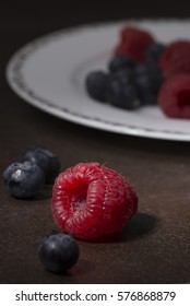 Close-up of a pink raspberry surrounded by blueberries, with a fruit ball in the background. Portrait format.