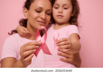 Close-up of a pink satin ribbons on blurred woman and girl hugging each other. World Breast Cancer awareness Day, 1 st October. Women's health, medical concept, World Cancer Day, Cancer Survivor Day. - Shutterstock ID 2036353640