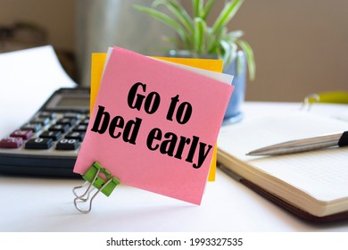 Closeup Pink Sticky Note paste it in a notebook setting an appointment. The words Go to bed early written on a white notebook to remind you an important appointment.