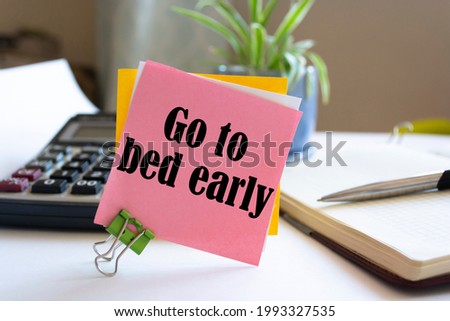 Closeup Pink Sticky Note paste it in a notebook setting an appointment. The words Go to bed early written on a white notebook to remind you an important appointment.