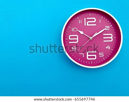 Closeup pink wall clock  set on blue background. The concept of 