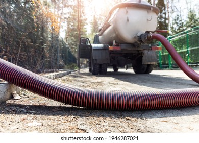 Close-up pipe hose of sewage truck car engine emptying home sewerage tank. Septic cleaning vacuum service and maintenance suburban countryside home. Suction vehicle cleaner machine pumping drainage