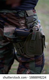 Close-up of a pistol in a holster on the leg of a soldier in camouflage uniform