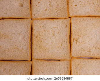 Close-up of plain white bread slices arranged in a neat, grid-like pattern, showing their soft texture and light golden crusts. Soft and fresh, breakfast, delicious, top view, full frame, background
