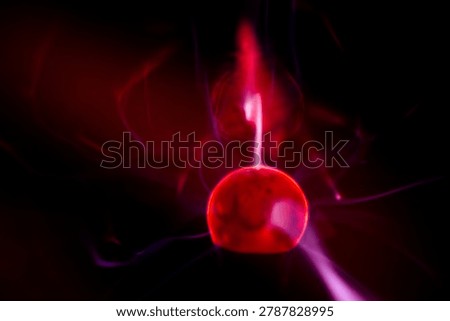 Close-up of a plasma ball globe glowing with red light and energy electricity rays on a black background
