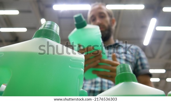 Close-up of plastic bottles with green cleaning agent\
and a male buyer takes\
one
