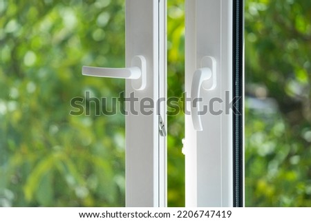 closeup of plastic pvc window with white metal frame and handle installed at house, view on blurred green trees. household concepts