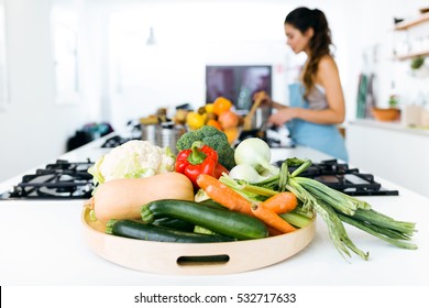 Close-up of plate of fresh vegetables and beautiful young woman cooking in the background.