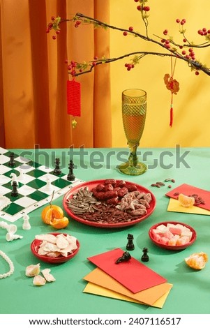 Close-up of a plate of ginger jam, a plate of colorful gummy candy, a plate of nuts, a chess set and lucky money envelopes displayed on a green table. Tet tea table concept.