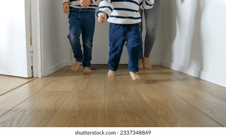 Closeup of playful little boys and their mother's feet running on wooden floor at home. A heartwarming concept of family love and happy childhood memories - Powered by Shutterstock