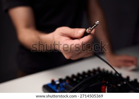 Closeup of plug approaching mixer input, hands steadying cable, colorful RCA and TRS connectors, tangled cable loom over console, matte knobs and labeled
