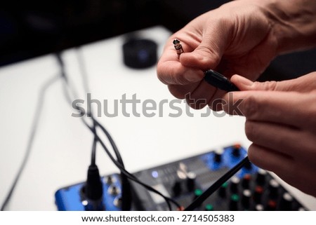 Closeup of plug approaching mixer input, hands steadying cable, colorful RCA and TRS connectors, tangled cable loom over console, matte knobs and labeled