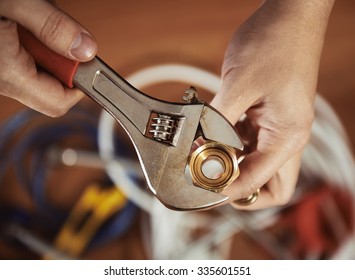 Close-up of plumber hands screwing nut of pipe with wrench over plumbing tools background.  Concept of repair and technical assistance. 