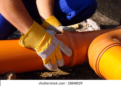 Closeup of plumber's hands assembling pvc sewage pipes in house foundation