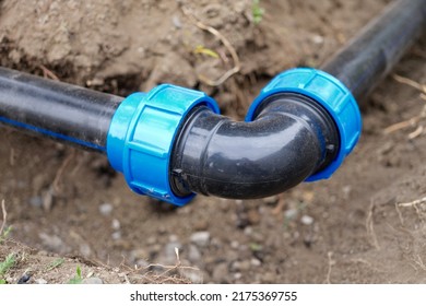 Close-up Of Plumbing Water Drainage Installation, Underground Irrigation System. Elbow Fitting And Pvc Pipes At Bend In Dirt Trench Outdoors