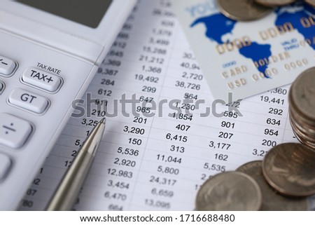 Close-up of plurality of numbers on spreadsheet in columns and rows facing left side. Calculator pen and cash money and credit card on accountant desk. Finance concept
