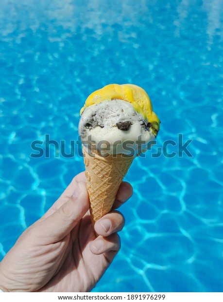 Closeup point of view mobile photography of\
male hand holding ice cream isolated on blue water of sunny\
outdoors pool\
background