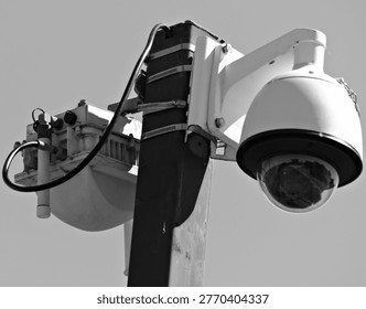 Close-up of a pole-mounted security camera and surveillance equipment against a clear blue sky