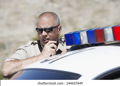 Closeup Of A Police Officer Using Two Way Radio By Police Car