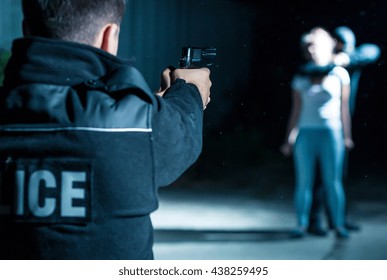 Close-up Of A Policeman Pointing His Gun At A Thief Holding A Hostage