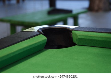 A close-up of a pool table corner pocket from inside, with the green felt and pocket lining.