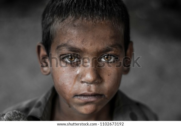 closeup of a poor staring hungry\
orphan boy in a refugee camp with a sad expression on his face and\
his face and clothes are dirty and his eyes are full of\
pain