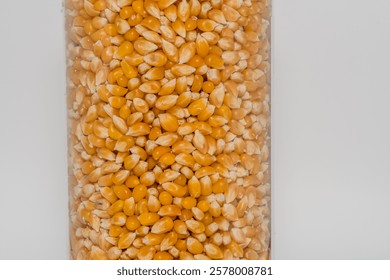 Closeup of popcorn kernels in clear container on white background.