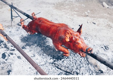 Closeup of the popular and delicious roasted pig known as "lechon baboy" skewered on a spit over burning charcoals on slow cooking or grilling. Selective focus. - Powered by Shutterstock